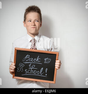 Die lustige pawky Schuljunge Teenager zeigt die schwarze Tafel mit der Aufschrift - zurück zur Schule Stockfoto