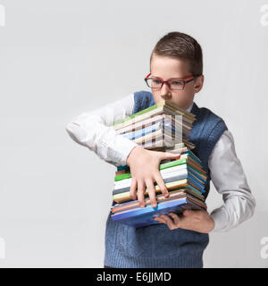 Die nette intelligente Schüler Teenager in einer Brille hält einen schweren Stapel Bücher. Stockfoto