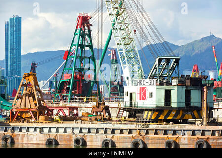 Schwimmkrane und Derrick Lastkähne In der Causeway Bay Typhoon Shelter, Hong Kong Stadtbild und die Berge dahinter. Stockfoto