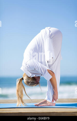 mittlere gealterte Frau in weiß beim Yoga am Strand Stockfoto