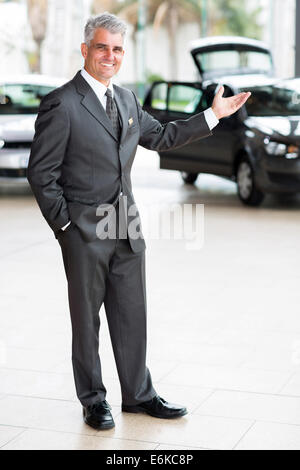 freundliche Autoverkäufer tut einladende Geste an Autohaus Stockfoto