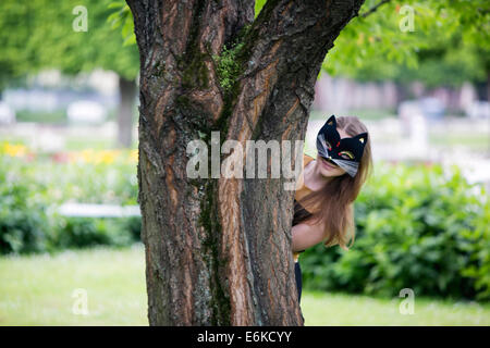 Junge Frau mit Maske versteckt sich hinter Eiche Stamm Stockfoto