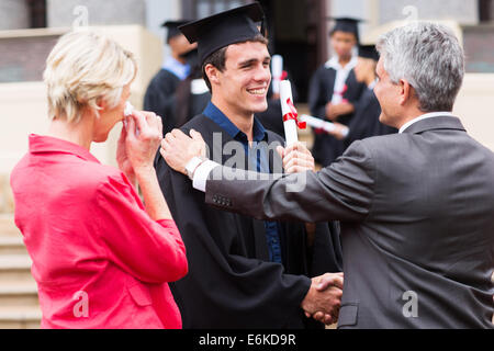 gut aussehend männlichen Absolvent wird von seinem Vater bei Abschlussfeier gratulierte Stockfoto