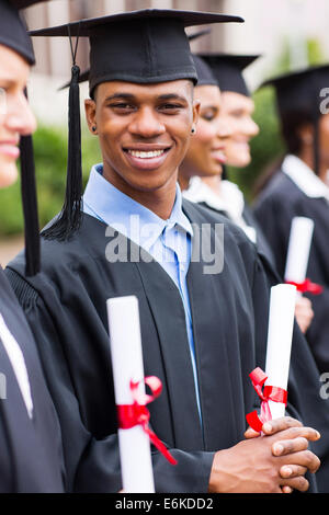 lächelnde afrikanische amerikanische männliche Absolventen mit Klassenkameraden in einer Reihe stehen Stockfoto