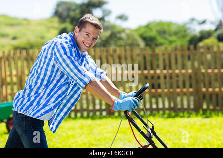 hübscher junger Mann schob Rasenmäher im Hausgarten Stockfoto