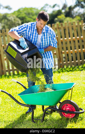 junger Mann Rasenmäher Rasen in einer Schubkarre nach dem Mähen entleeren Stockfoto