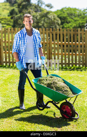 junger Mann schob Schubkarre voller Gras nach der Reinigung Hinterhof Stockfoto