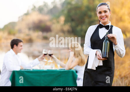 attraktive Kellnerin mit einer Flasche Wein vor Kunden Stockfoto