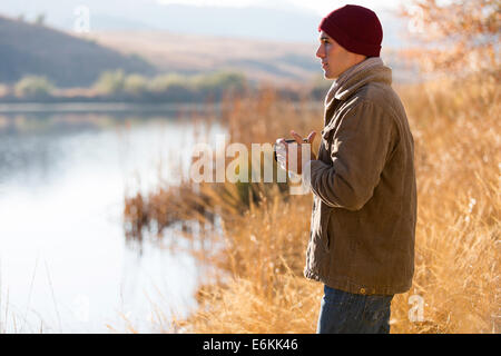 nachdenklicher Mann See stehen und Kaffeetrinken im Herbst Stockfoto