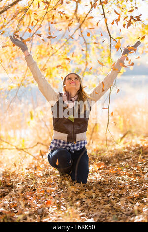 glückliche junge Frau wirft Herbstlaub im Wald Stockfoto