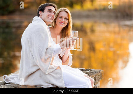 schöne junge Paar mit Wein am See bei Sonnenuntergang Stockfoto