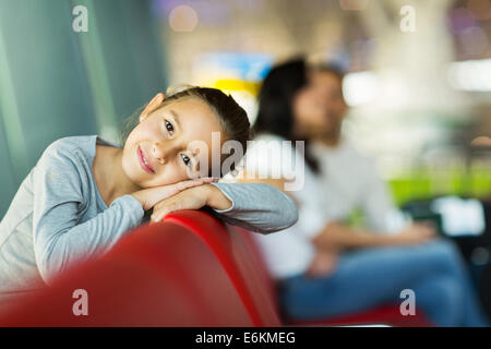 niedliche kleine Mädchen auf Bank am Flughafen mit den Eltern im Hintergrund Kopf liegend Stockfoto