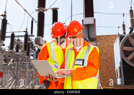 zwei moderne Elektrotechniker mit Laptop im Umspannwerk Stockfoto