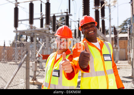 zwei fröhliche Techniker geben Daumen nach oben im Umspannwerk Stockfoto