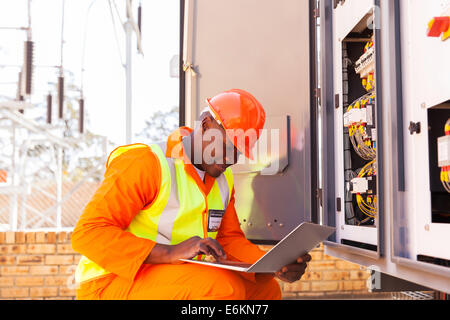 schöne afrikanische Elektrotechniker arbeiten am Laptop neben Trafo Stockfoto