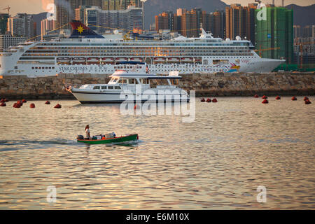 Kontrastierende Schiffe. Kleines Boot in der Causeway Bay Typhoon Shelter und ein Kreuzfahrtschiff, das durch den Victoria Hafen und Hong Kong Skyline hinter sich. Stockfoto