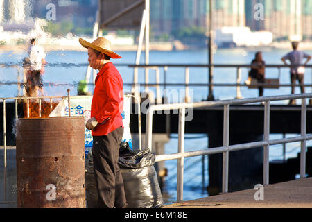 Die brennenden Fass. Chinesischer Mann In einem Strohhut während der Abfälle in einem Ölfass am Pier North Point, Hong Kong. Stockfoto