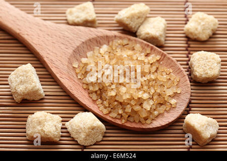 Brauner Rohrzucker Kristalle in einem Holzlöffel auf Bambus-Serviette. Closeup. Stockfoto