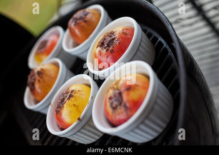 Rösten Sie Äpfel in weißer Keramik Tassen auf einem Kugelgrill Grill. Stockfoto