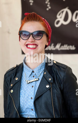 lächelnde junge Frau mit rot gefärbten Haaren kümmert sich um einen Stand auf der siegreichen Festival 2014 Southsea England uk Stockfoto