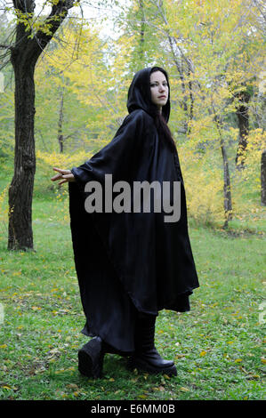 Schwarz mit Kapuze Dryade Frau in den herbstlichen Wald, dich beim gehen, als ob winkte zurück Stockfoto