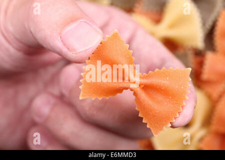Rote Nudeln Farfalle in den Fingern über bunte Pasta Farfalle Hintergrund. Close-up. Stockfoto