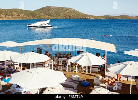 Urlauber entspannen am klaren, blauen Meer, Boote beobachten und genießen Getränke im Beyaz Beach Club, Bodrum Türkei Stockfoto