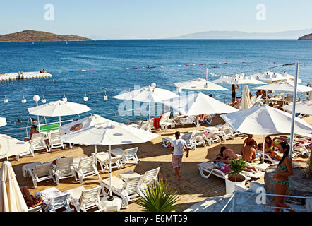 Urlauber entspannen am klaren, blauen Meer, Boote beobachten und genießen Getränke im Beyaz Beach Club, Bodrum Türkei Stockfoto