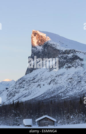 Mount Skerfe im Sarek Nationalpark, Winterlandschaft mit die Sonne auf den Gipfel und einer alten Scheune vor in der mo Stockfoto