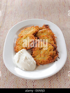 Kartoffelpuffer mit saurer Sahne auf weißen Teller Stockfoto