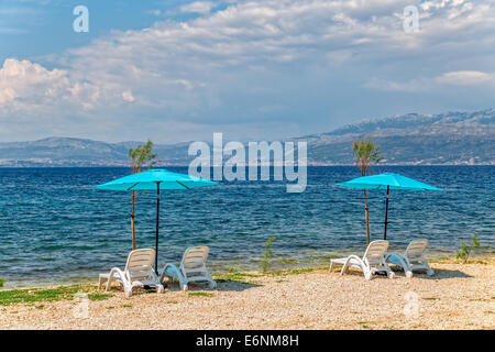 Vier liegen und zwei Sonnenschirme am Strand am Meer in Supetar auf der Insel. Stockfoto