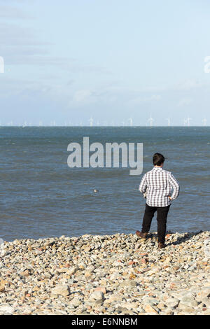 Ein Teenager stehen auf der Kiesstrand von Llandudno, mit Blick auf die Windkraftanlagen des Windparks Gwynt y Môr und Rhyl Flats. Stockfoto