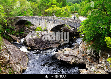 Ein Tourist, der Blick auf ein Handy auf Thomas Telfords historischen Straßenbrücke, Invermoriston, Schottisches Hochland, Schottland Stockfoto