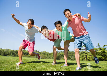 Vier fröhliche junge Männer stehen Arm in Arm auf dem Rasen Stockfoto