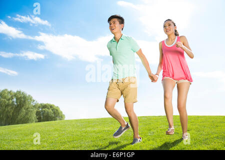 Fröhliche junge Paar Hand in Hand laufen auf dem Rasen Stockfoto