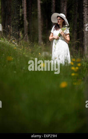 Frau im weißen Kleid mit weißen Hut mit Wäldern Blumenstrauß in Händen im Wald spazieren Stockfoto