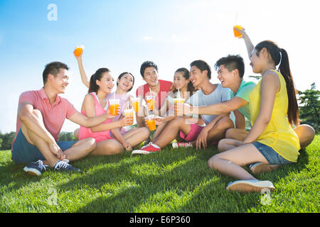 Fröhliche junge Erwachsene halten Saft sitzen auf Rasen Stockfoto