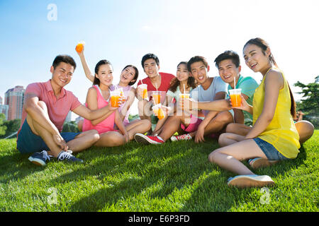 Fröhliche junge Erwachsene halten Saft sitzen auf Rasen Stockfoto