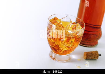 Alkoholisches Getränk in ein Glas mit Eiswürfeln und eine Flasche und Korken auf weißem Hintergrund Stockfoto