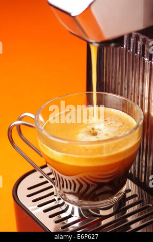 Nahaufnahme einer Glas-Tasse in einer Kaffeemaschine über orange Hintergrund Stockfoto