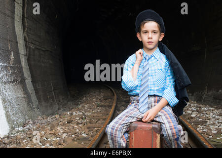Kind in Vintage-Kleidung sitzt auf Eisenbahn Straße vor einem Tunnel. Stockfoto