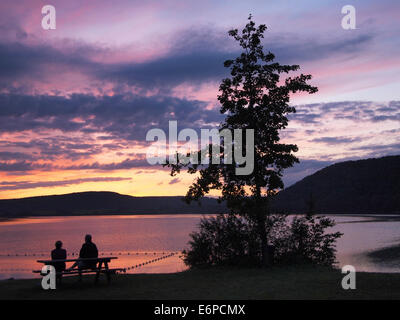 Lac de Chalain Sonnenuntergang, Jura, Frankreich mit zwei Silhouette Leute sitzen auf einem Picknick-Tisch, Blick in die Ferne Stockfoto