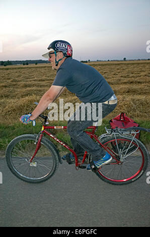 Mann Alter 38 das Tragen eines Helmes mit seinem Fahrrad entlang einer polnischen Landstraße in der Abenddämmerung. Zawady Polen Stockfoto