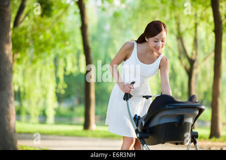 Junge Frau mit ihrem Baby im Kinderwagen spazieren Stockfoto