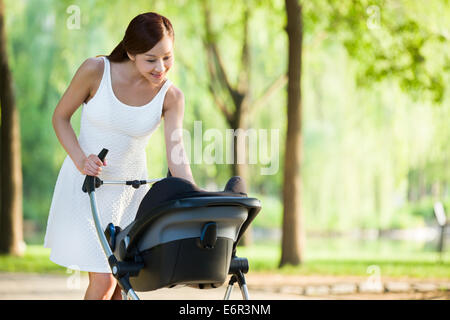 Junge Frau mit ihrem Baby im Kinderwagen spazieren Stockfoto