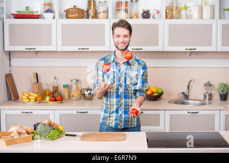 Fröhlicher junge Mensch jonglieren Tomaten während der Zubereitung von Speisen in der Küche Stockfoto