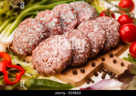 Rohe Frikadellen auf ein Schneidebrett und Zutaten. horizontale. Close-up Stockfoto