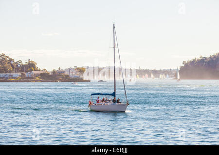 Eine Yacht und andere Boote Segeln im Hafen von Sydney an einem sonnigen Wintertag genießen. Stockfoto