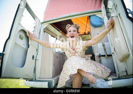 Eine Frau, gekleidet in Retro-50er Jahre amerikanische Hausfrau Stil Sommer Kleid Kleid sitzen posiert in einem klassischen Periode Wohnmobil UK Stockfoto