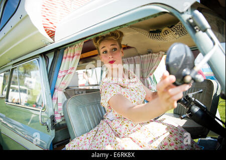 Eine Frau, gekleidet in Retro-50er Jahre amerikanische Hausfrau Stil Sommer Kleid Kleid sitzen posiert in einem klassischen Periode Wohnmobil UK Stockfoto